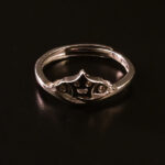 "Sterling silver ring featuring a crown design with a smiley face at the center, displayed on a dark background."