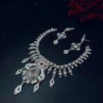 Handcrafted silver-plated necklace set with matching earrings, adorned with red and green enamel teardrop accents, displayed on a black background.