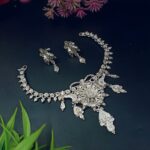 Elegant handcrafted silver necklace set with matching earrings on a dark background, surrounded by flowers.