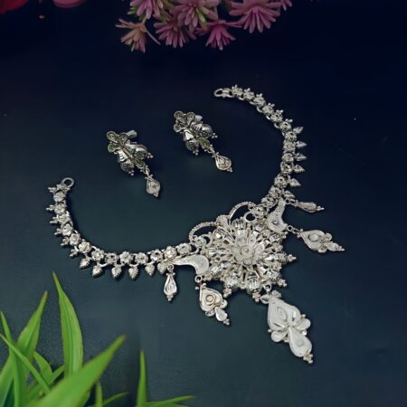 Elegant handcrafted silver necklace set with matching earrings on a dark background, surrounded by flowers.