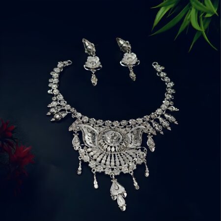 A handcrafted silver-plated necklace with matching earrings, elegantly displayed on a dark velvet background with red and green floral accents.