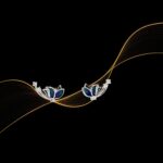 A pair of silver earrings featuring a stylized floral design with blue and teal enamel petals and small clear stones along the curved stems.