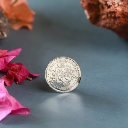 Jain silver coin with Om and Swastika symbols placed on a brown surface