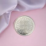 10 gram pure silver coin with Swastik symbol engraved, 999 purity, placed on pink background with white fabric.