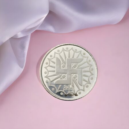 10 gram pure silver coin with Swastik symbol engraved, 999 purity, placed on pink background with white fabric.